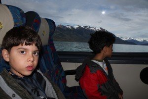 duas crianças em barco com lago e montanhas nevadas ao fundo
