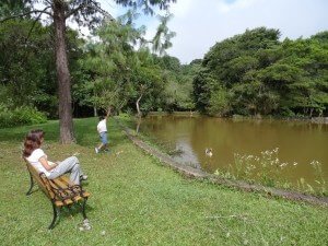 mulher sentada em banco e menino brincando perto de lago